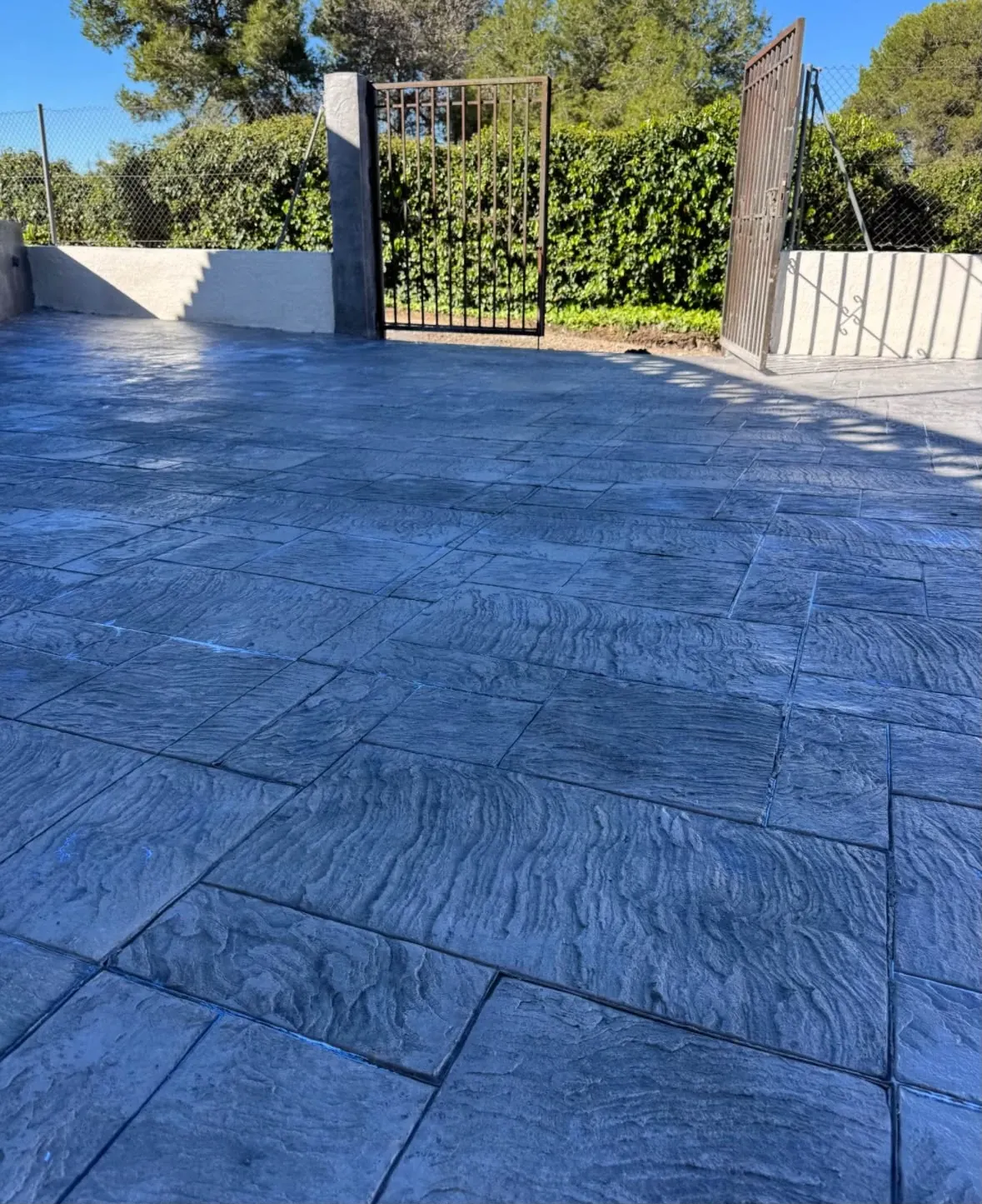 Patio de hormigón impreso gris azulado junto a una cancela