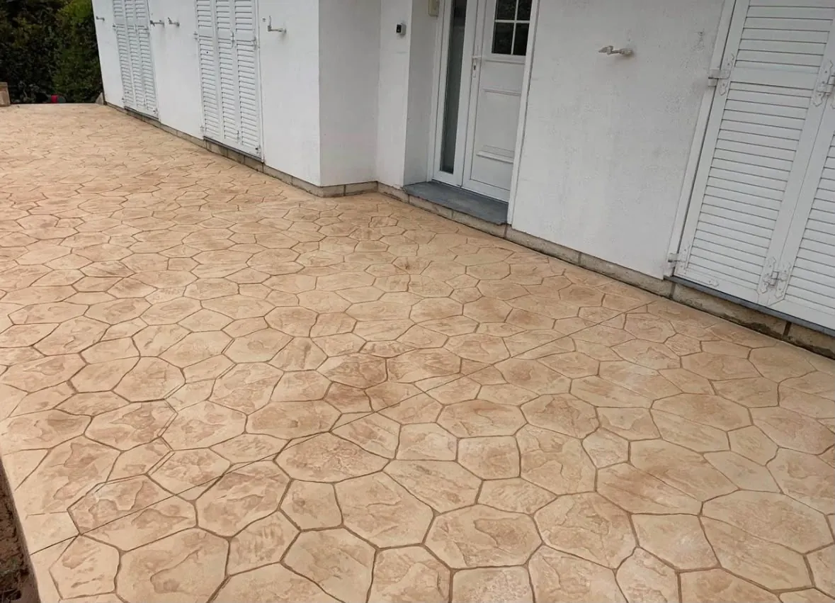 Terraza de hormigón impreso en piedra natural color crema junto a una casa blanca